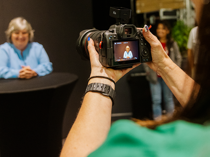 A photographer shooting a seated guest on a DSLR in Curator Photography Mode, the portrait visible on the camera's rear screen.