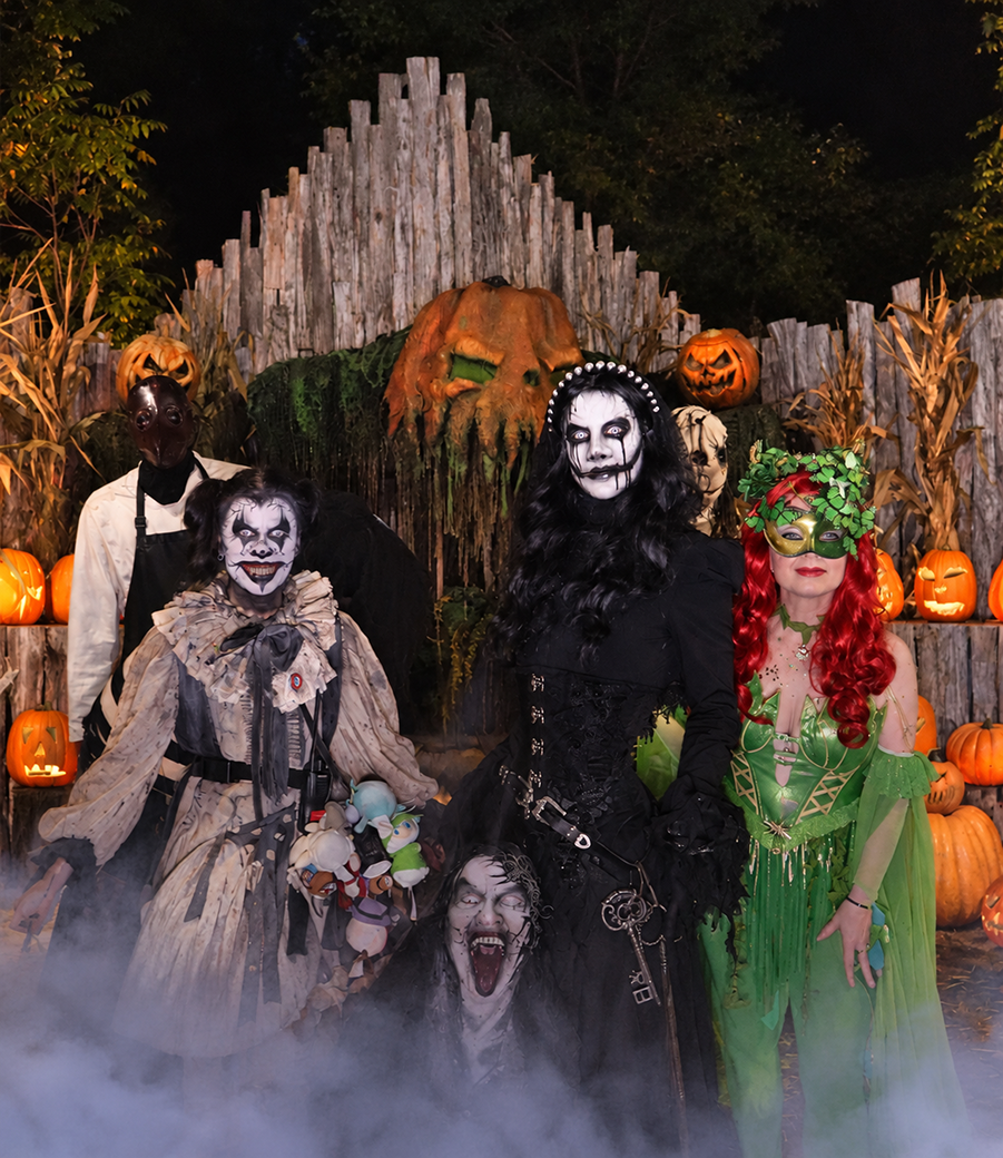 Costumed scare actors posed in front of a pumpkin-covered fence in the fog at a haunted attraction.